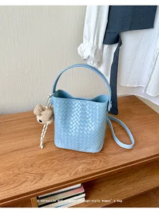 Light blue woven bucket bag with bear pendant on wooden surface.