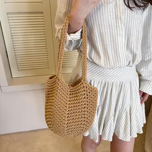 Detailed view of a hand-knitted straw underarm bag styled with a summer dress.