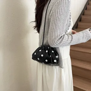 Detail shot of a black polka dot dumpling shoulder bag worn with a grey cardigan.