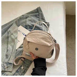 Vista detallada de un bolso bandolera de nailon beige con correa ajustable y logo.