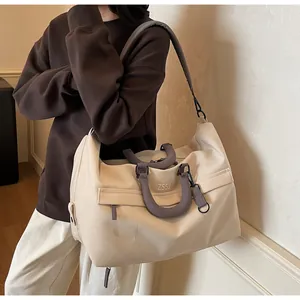 Grand sac de voyage beige avec poignées grises porté par un mannequin en intérieur