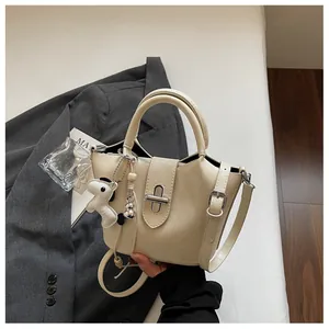 Détail d'un sac seau crème avec un accessoire chien posé sur un fond de blazer gris élégant