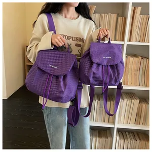 Two sizes of purple checkered backpacks displayed on a model in a casual indoor setting