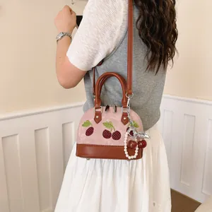 Bolso bandolera rosa elegante con bordado de cerezas y un detalle de colgante de perlas fino.