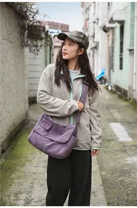 Outdoor lifestyle shot of a large capacity purple canvas messenger bag worn by a model