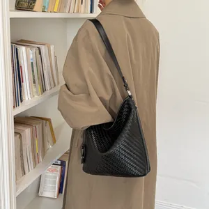 Detailweergave van een zwarte geweven emmertas met een chique beige trenchcoat
