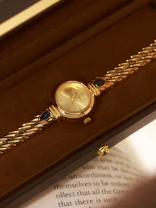 Primer plano de reloj de lujo para mujer en oro con circonitas azules y correa de cadena.