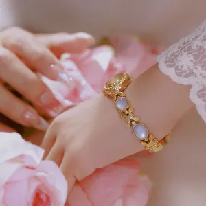 Elegante reloj de pulsera vintage dorado con piedras lilas sobre una manga de encaje blanco