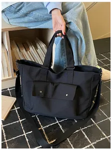 Detailed view of a large black canvas tote bag held by a model in a casual indoor setting