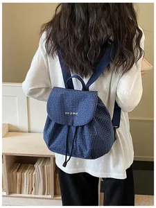 Rear view of a model wearing a stylish blue checkered backpack in a minimalist room
