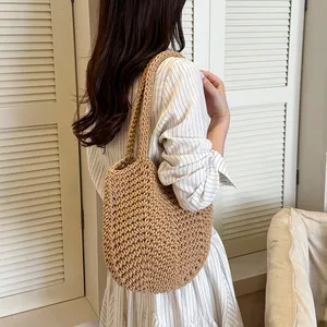 Detail view of a brown hand-woven crochet shoulder bag carried by a model in a striped dress.