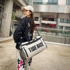 Detailweergave van de stijlvolle beige TIDE RICE duffeltas gedragen in een stedelijke omgeving