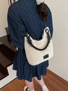 Chic beige woven hobo bag with unique black beaded strap carried by model stylishly