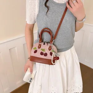 Elegante bolso bandolera rosa y marrón con bordado de cerezas y colgante de perlas en modelo.