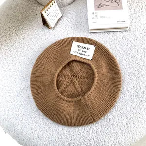 Close-up of a brown knit beret with a Season 13 letter patch on a white fuzzy rug.