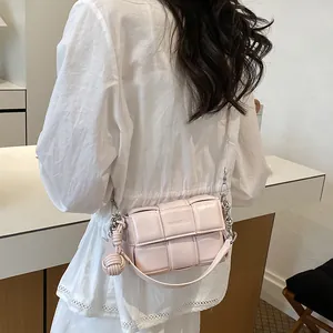 Detailed view of a light pink woven square bag with a chain strap worn by a model