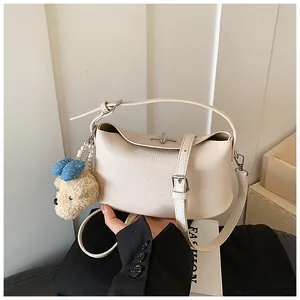 Primo piano di una borsa a secchiello in pelle crema con un grazioso ciondolo a orsetto
