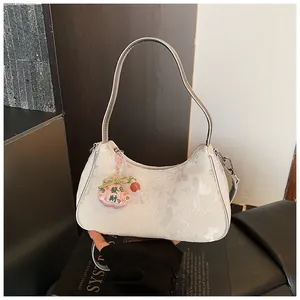 Close-up detail of white underarm bag with butterfly patterns and charm
