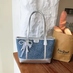 Blue denim tote bag with silver handles and a decorative white pearl lace bow charm