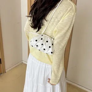 Close-up of white polka dot dumpling crossbody bag styled with casual yellow knit outfit