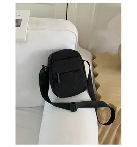 Detailed view of a black minimalist nylon crossbody phone bag styled on a white sofa