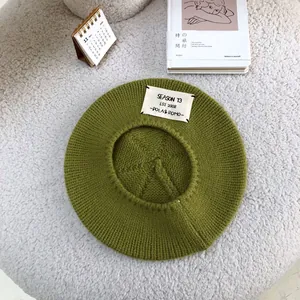 Close-up detail of a green knitted wool beret with a vintage style lettered patch design