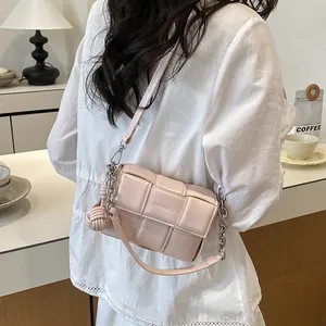 Detailed view of a pink woven padded crossbody bag with chain and knotted charm.