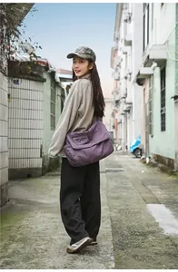 Purple canvas messenger bag detail worn by a model in an urban outdoor setting