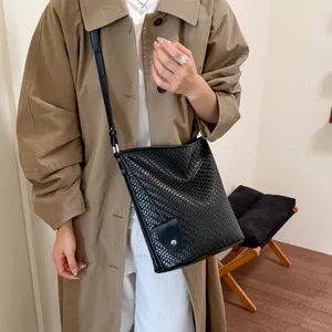 Lifestyle-detail van een vrouw die een zwarte vintage geweven emmertas en trenchcoat draagt