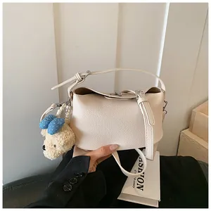 Elegant cream pebbled leather bucket handbag featuring a charming plush teddy bear pendant detail