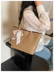 Detail of large brown tote bag with geometric embossed pattern and decorative ribbon scarf