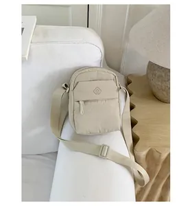 Minimalist beige crossbody bag displayed on a white sofa in a cozy interior setting.