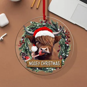 Close-up detail of a round acrylic Christmas ornament featuring a cute Highland cow in a Santa hat