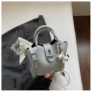 Sac seau bleu clair élégant avec breloque cheval et bandoulière sur fond de blazer