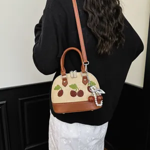 Detalle del bolso de lona beige con bordado de cerezas y colgante de perlas