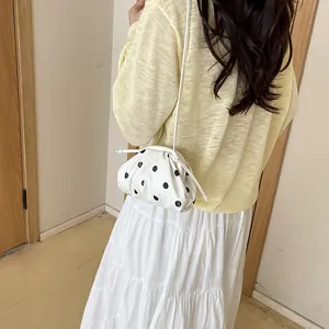 White drawstring pouch bag with black polka dots worn on shoulder for summer casual style.