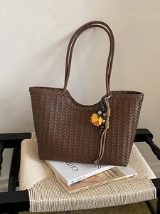 Bolso de mano de cuero tejido marrón con un amuleto decorativo de flor y borlas