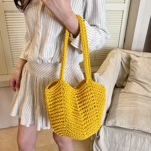 Vibrant yellow hand-knitted shoulder tote bag held by a model in a cozy indoor setting.