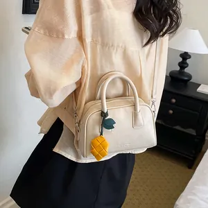 Stylish cream faux leather pillow bag with lemon charm carried by a woman in a room