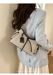 Bolso bajo el brazo beige con ribete negro llevado por una modelo con blazer azul claro