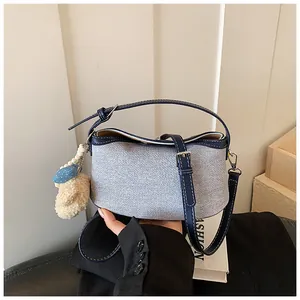 Close-up detail showing the denim fabric texture and plush bear charm on this blue bucket bag