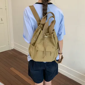 Mochila casual caqui con cordón ajustable llevada por una modelo en entorno cotidiano.