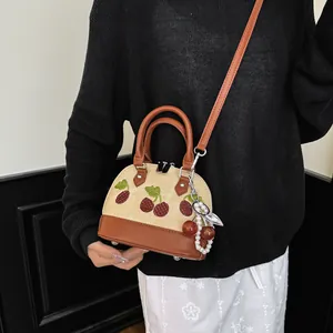Primer plano del bordado de cerezas y el colgante de perlas en un bolso elegante.