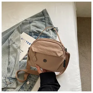 Bolso bandolera de nailon caqui versátil con etiqueta CHUANGMI sobre fondo de mezclilla.