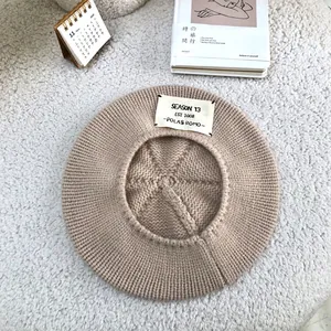 Detailed top-down view of a cozy beige knitted beret with a stylish white letter patch.
