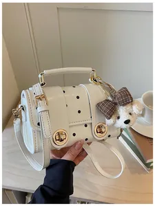 Detail view of a white polka dot handbag with a cute plush dog charm decoration.