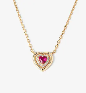 Close-up detail of gold heart necklace with red gemstone and sparkling accents
