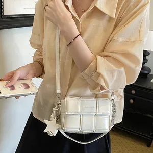 Detail view of a creamy white woven crossbody bag with star charm worn by a model.