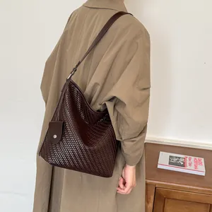 Detailweergave van donkerbruine gevlochten hobo-tas gestyled met een klassieke beige trenchcoat
