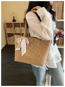Close-up detail of khaki tote bag featuring geometric embossed pattern and silk scarf accessory